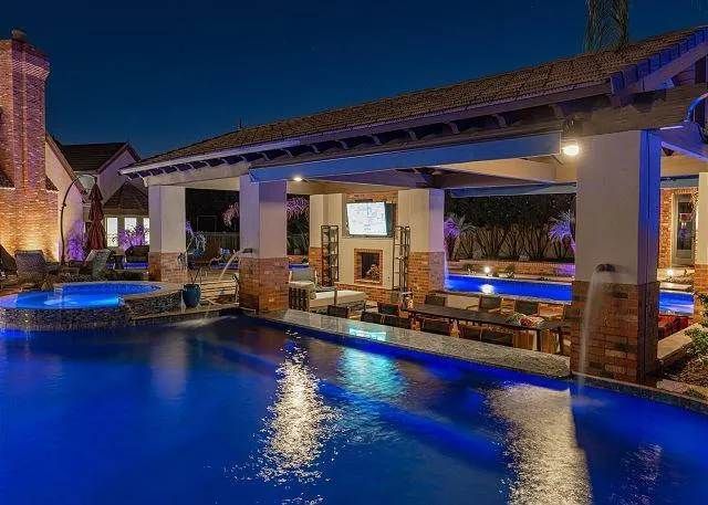 Poolside bar at night with blue-lit pool, brick columns, fireplace, and seating area.