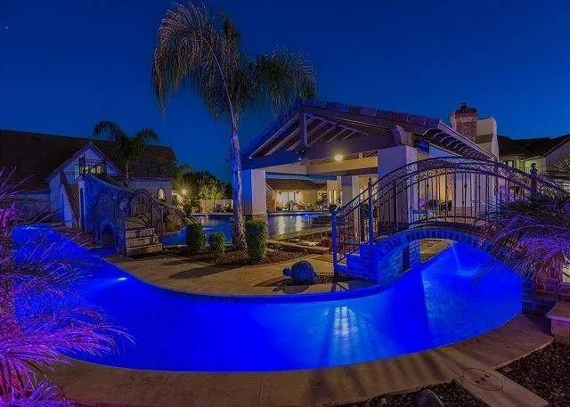 Pool area at night illuminated with blue lights, bridge to a covered patio.