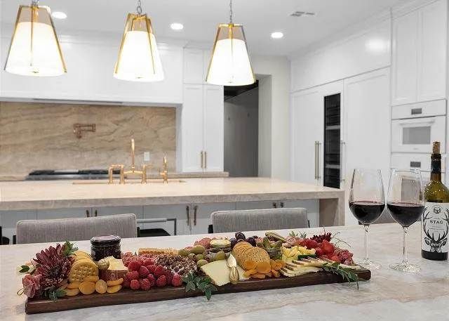Charcuterie board with wine glasses and bottle on a kitchen island, under pendant lights.