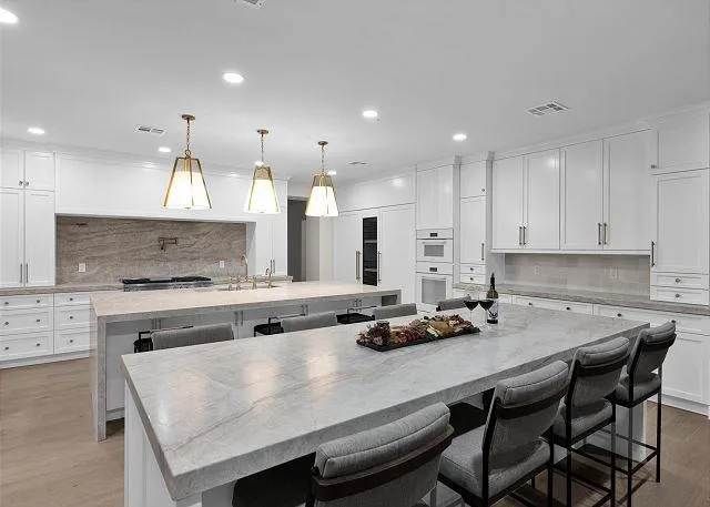 Modern white kitchen with two islands, bar seating, and pendant lights.