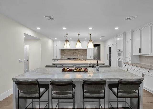 Modern white kitchen with two islands, bar seating, and hanging lights.