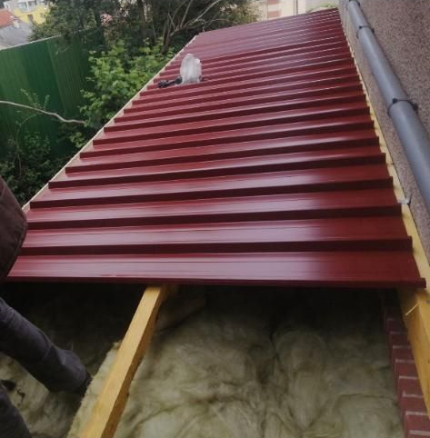 Installation d'une toiture en tôle ondulée rouge. Charpente en bois avec isolation visible.