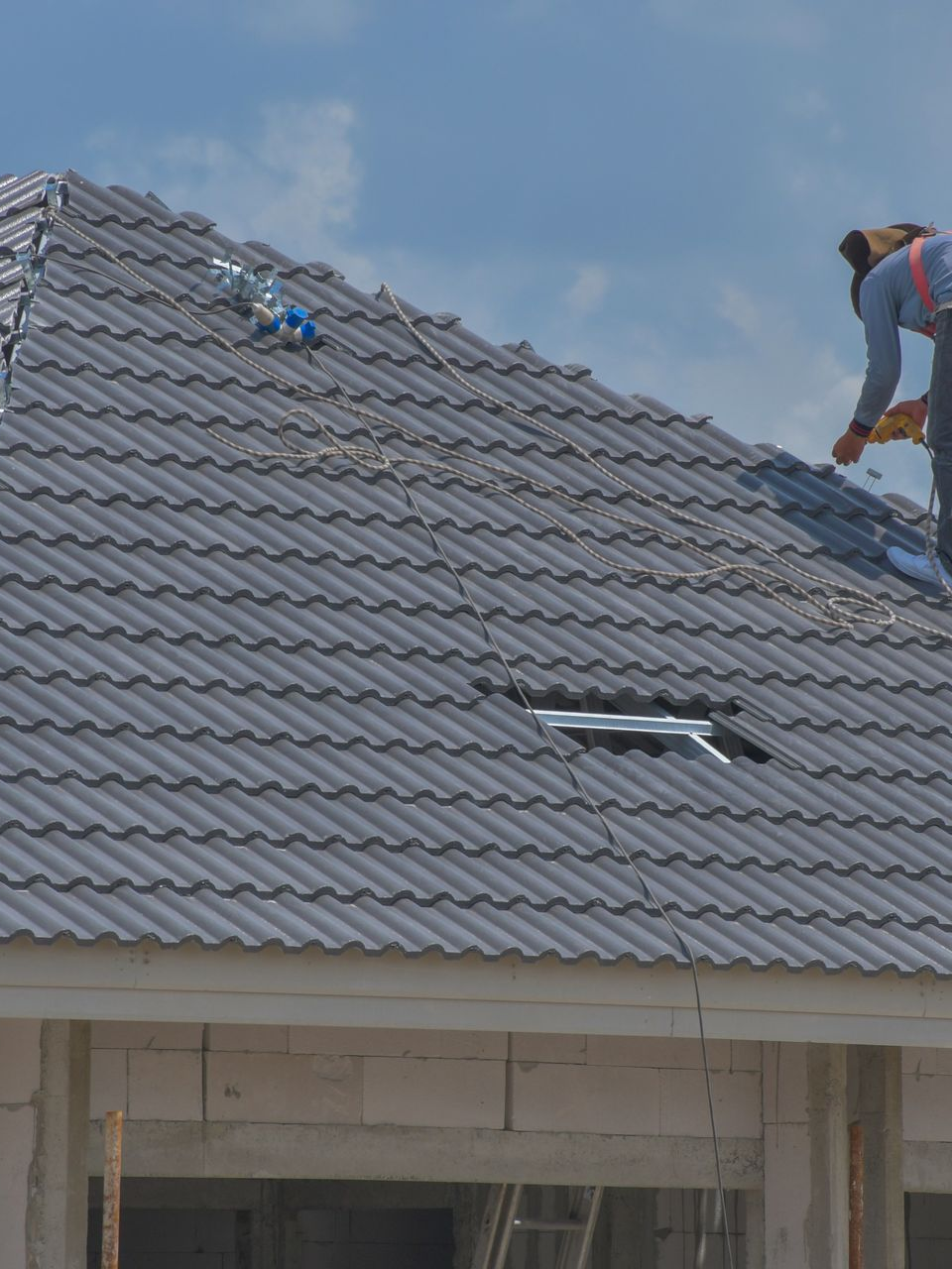 Une personne installe des tuiles gris foncé sur un toit.
