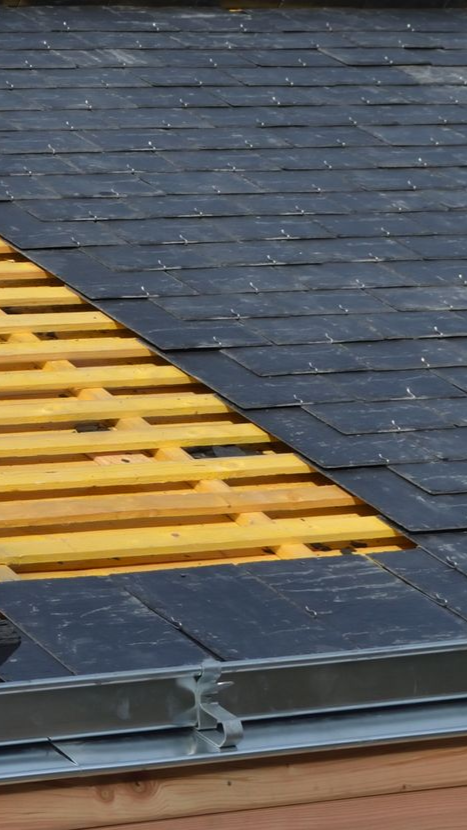 Toiture avec chevrons en bois partiellement apparents et bardeaux noirs, solins métalliques visibles.