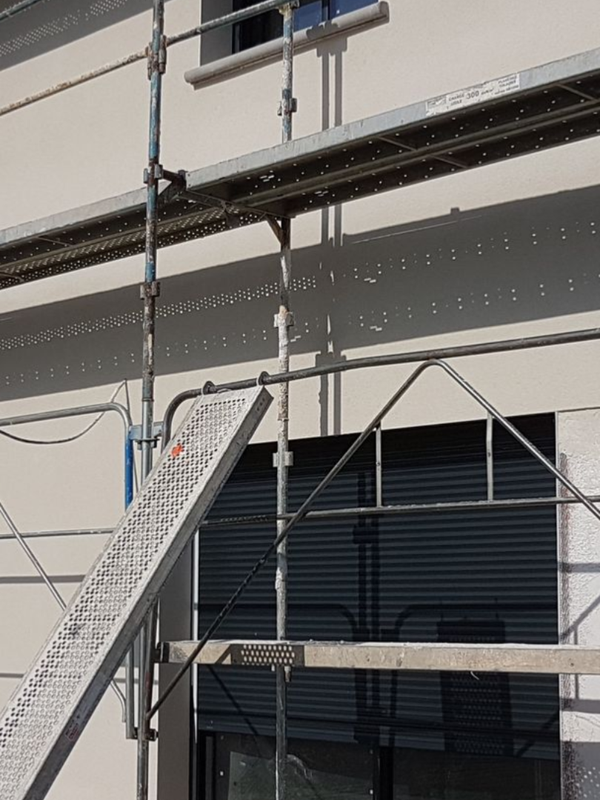 Échafaudage fixé à la façade d'un bâtiment vitré. Un escalier mène à une plateforme de travail.