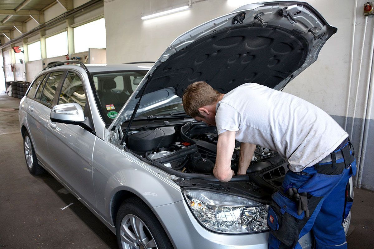 Ein Mann schaut unter die Motorhaube eines silbernen Autos