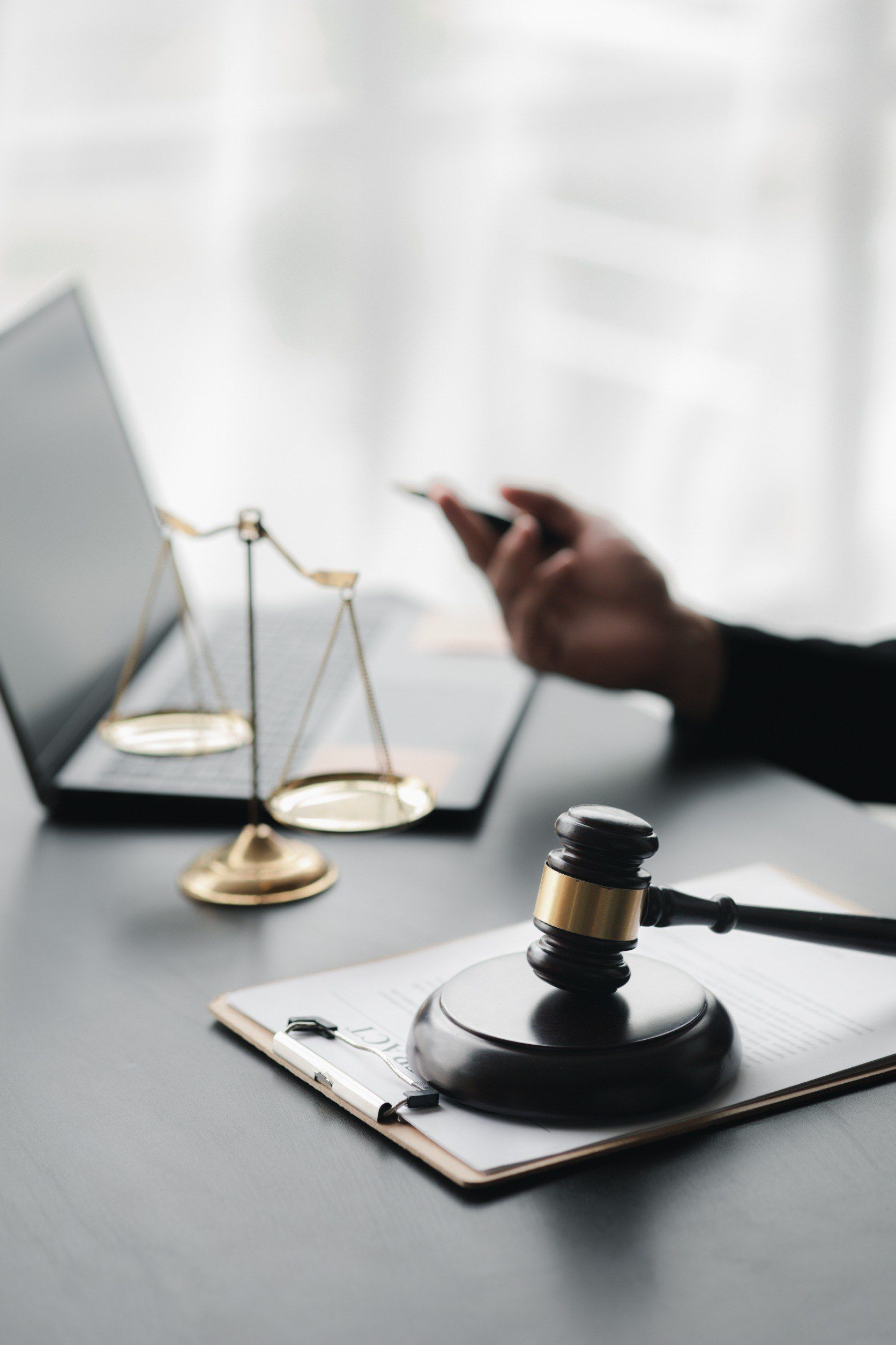 Un mazo de juez está en un portapapeles junto a una balanza de justicia y una computadora portátil.