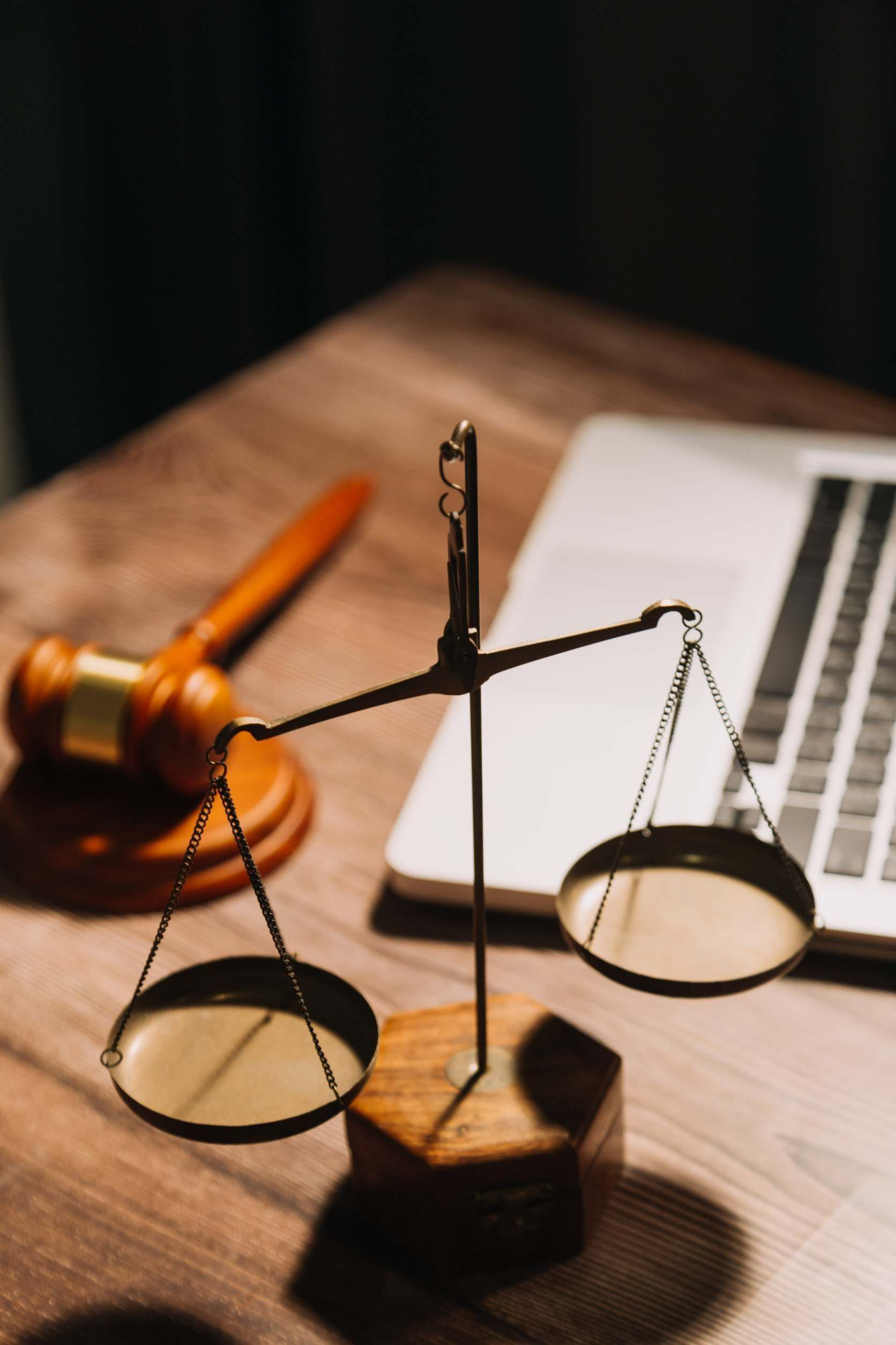 Una balanza de la justicia se encuentra sobre una mesa de madera junto a una computadora portátil.