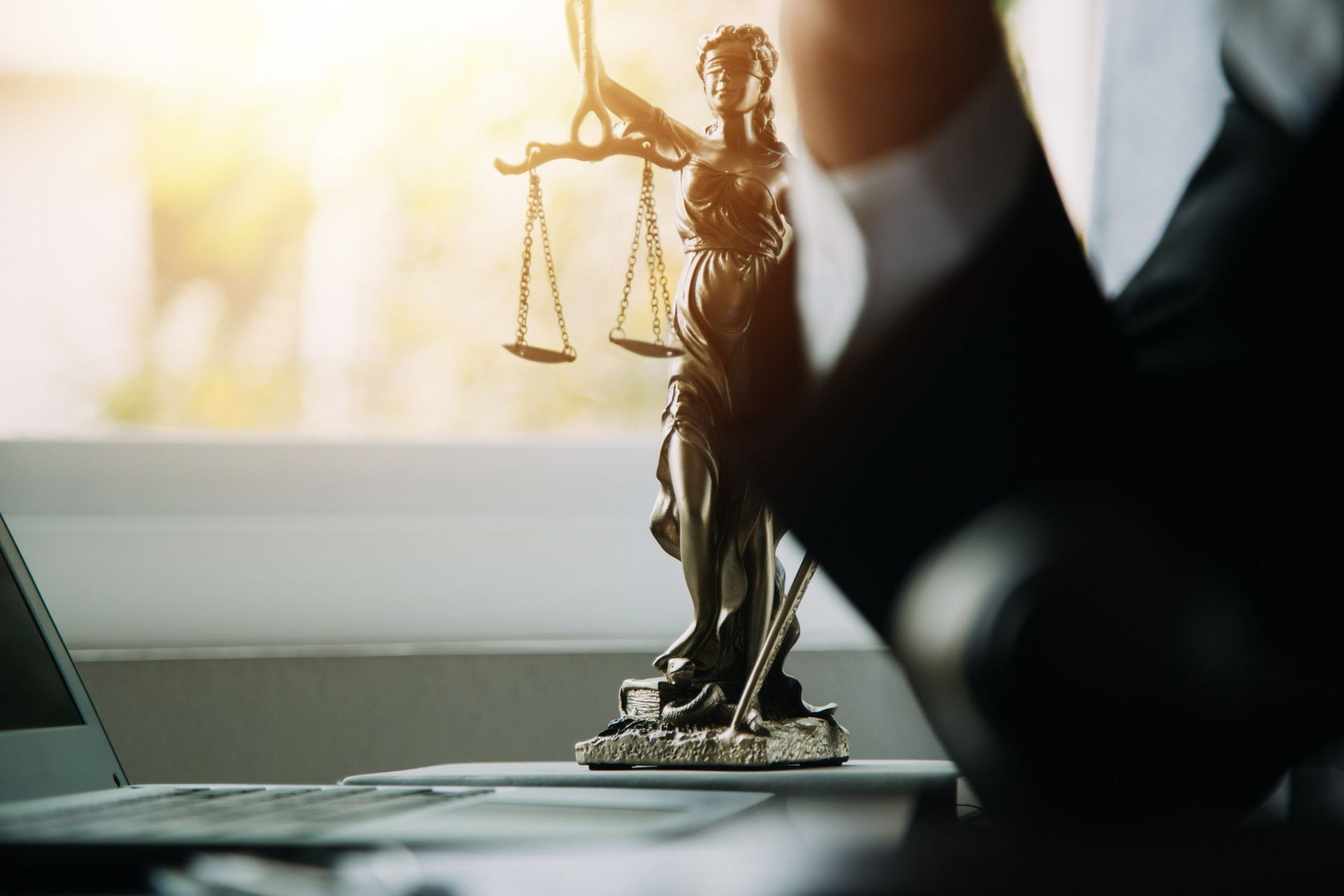 Una estatua de la justicia está sentada en un escritorio al lado de una computadora portátil.