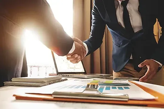 Dos hombres de negocios se dan la mano sobre una mesa.