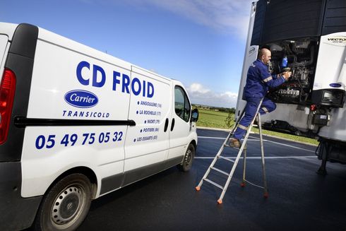 Un technicien sur une échelle effectue l'entretien du groupe frigorifique d'un camion à côté d'une camionnette blanche de CD FROID