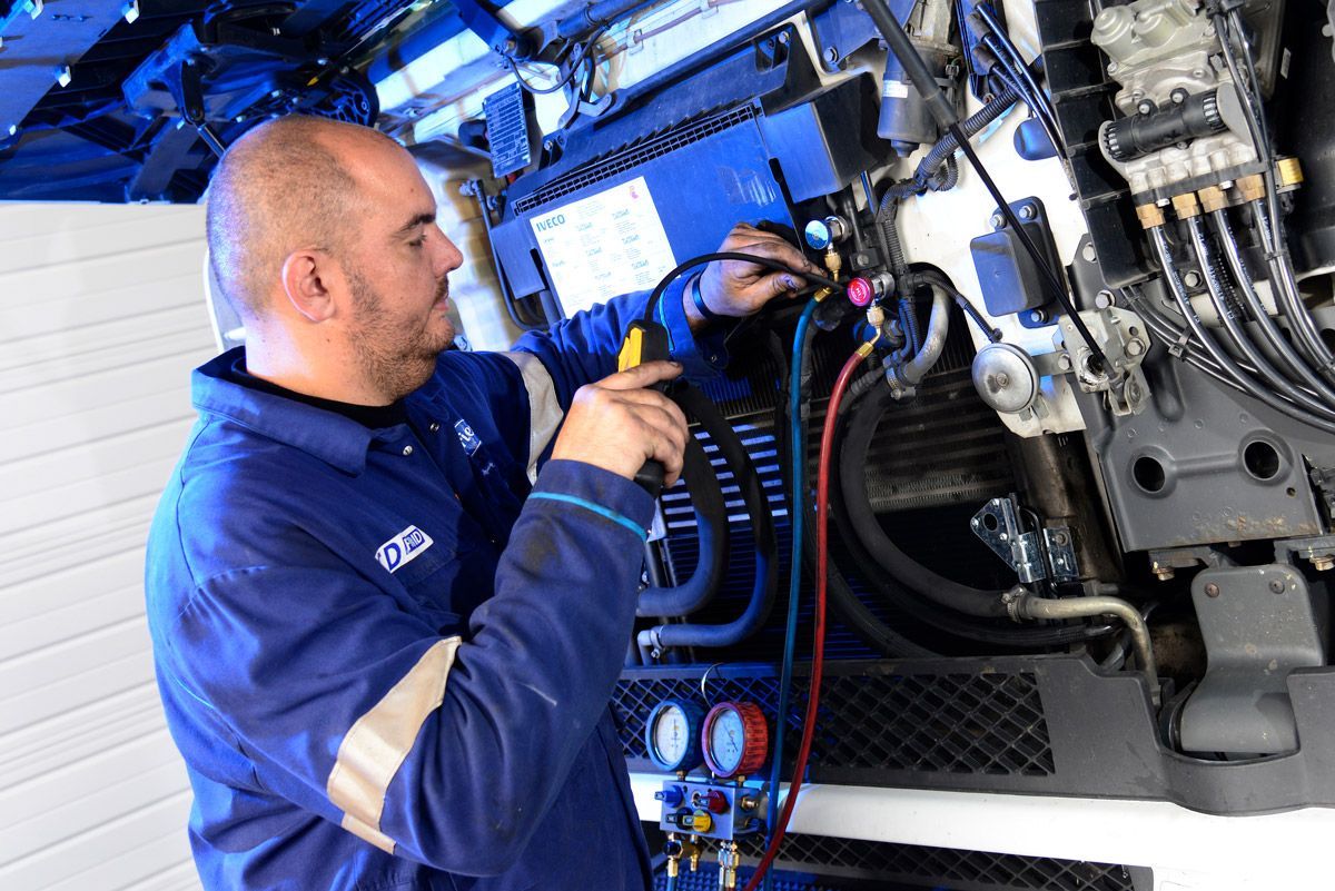 Un technicien en combinaison bleue inspecte des machines à l'aide d'un outil dans un atelier