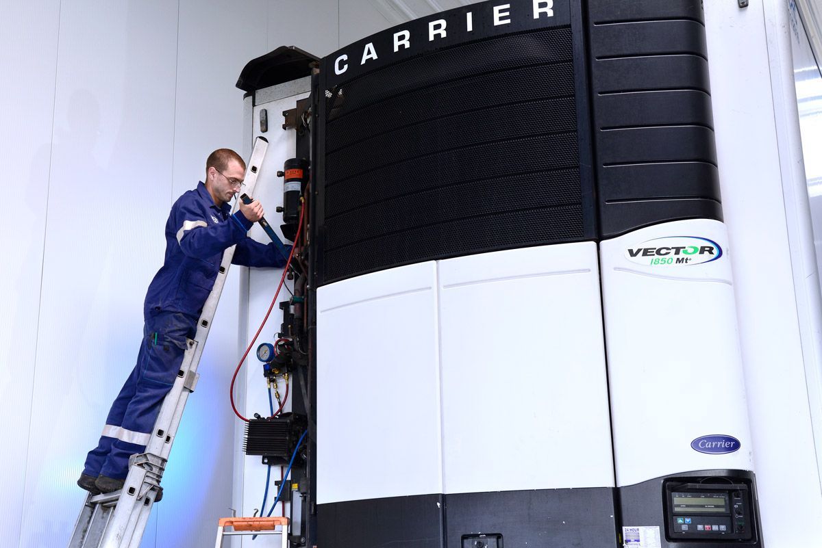 Technicien sur une échelle effectuant l'entretien d'une grande unité de climatisation Carrier à l'intérieur
