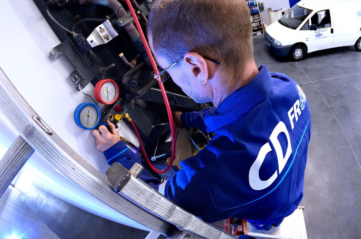 Un technicien en uniforme bleu vérifie les manomètres d'un équipement de CVC dans un atelier