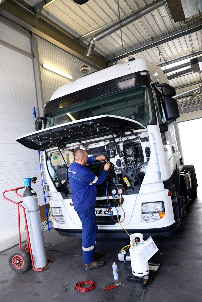Un mécanicien en salopette bleue répare un camion blanc dans un atelier