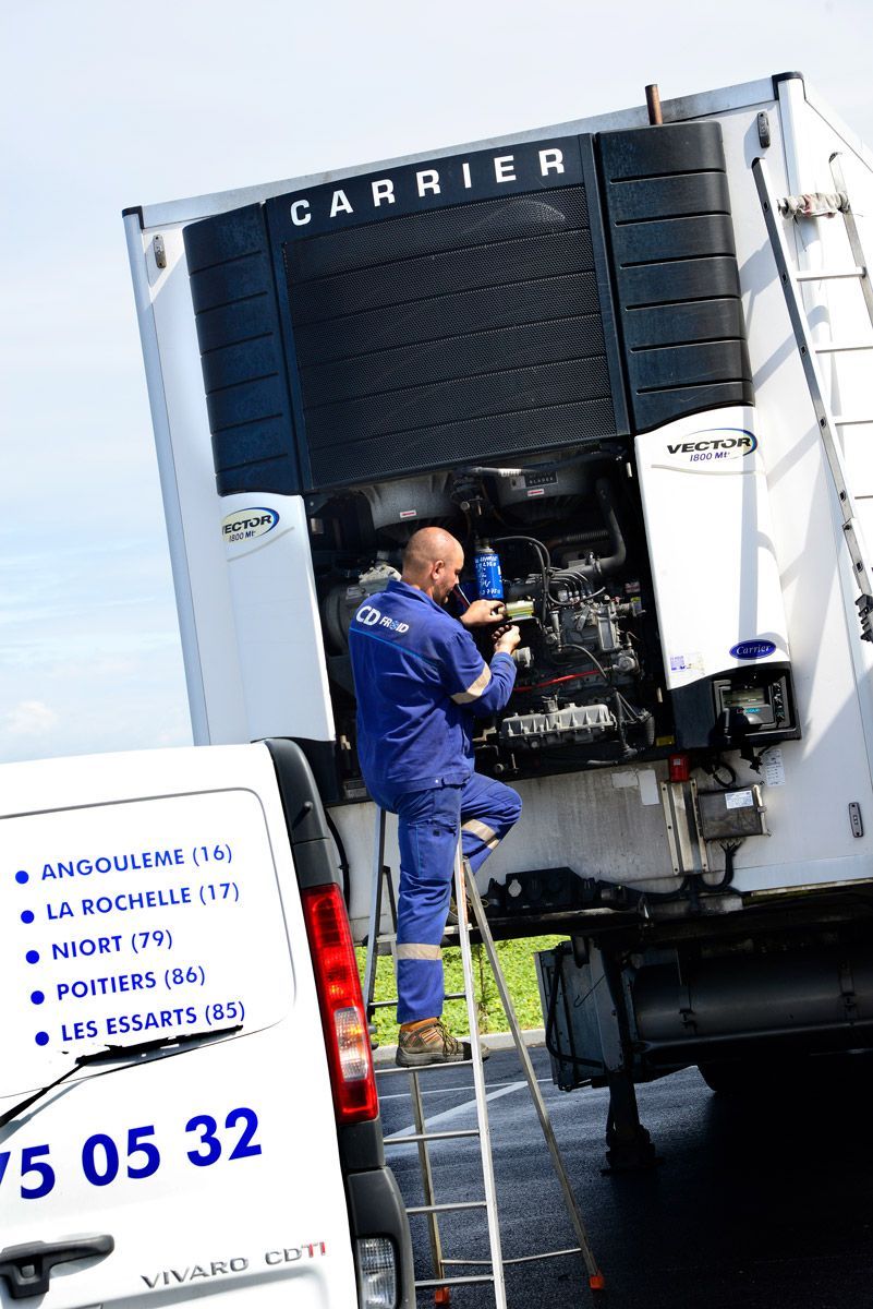 Un ouvrier, debout sur une échelle, effectue la maintenance d'un grand groupe frigorifique de camion Carrier à l'extérieur