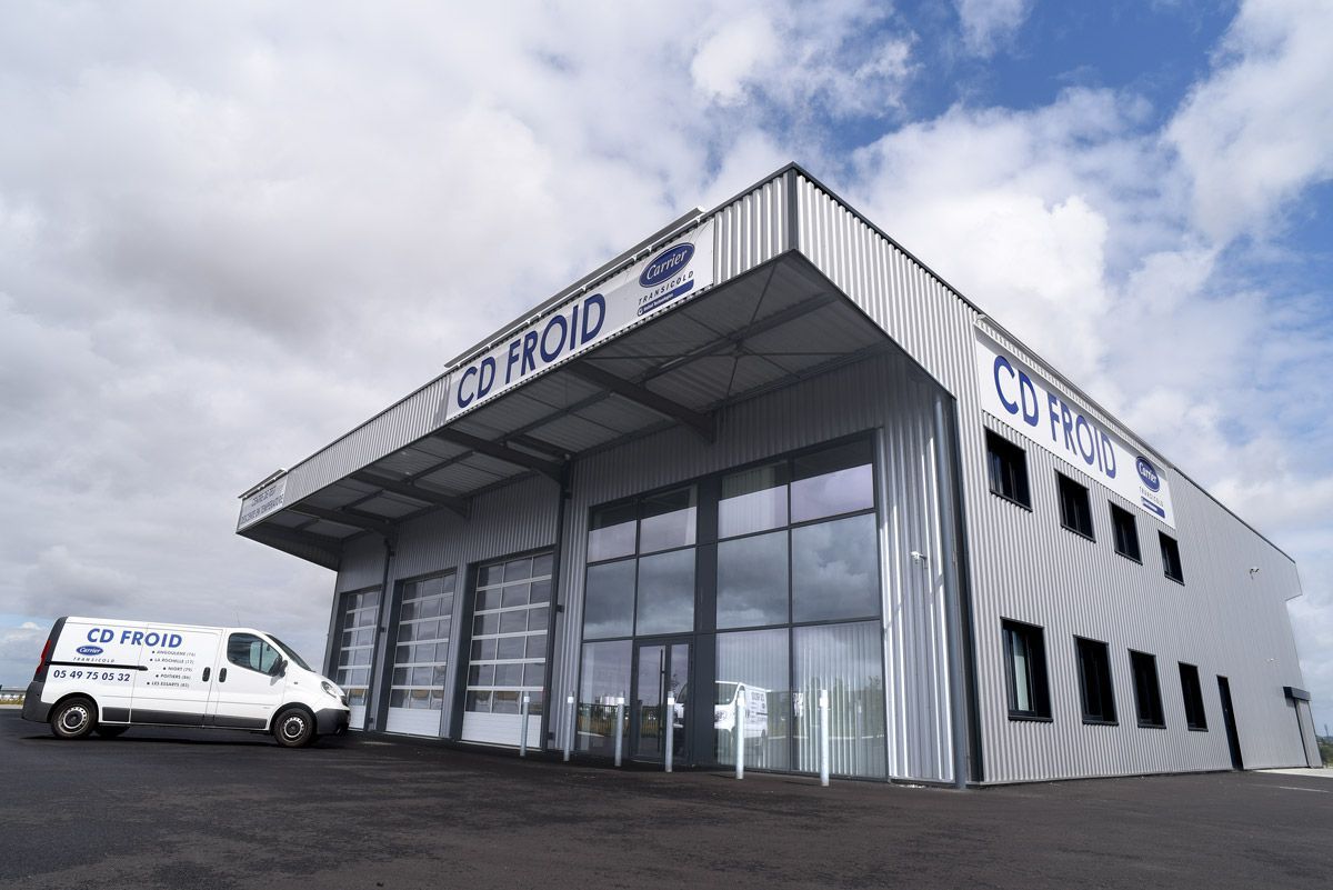 Bâtiment industriel moderne avec une grande entrée vitrée et une camionnette blanche garée devant