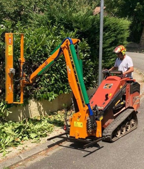 Un homme travaille sur un petit tracteur rouge pour tailler une haie de laurier.
