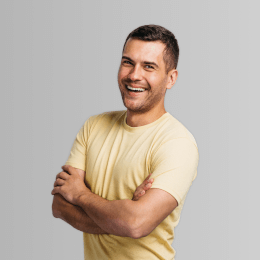 Ein Mann in einem gelben T-Shirt steht mit verschränkten Armen da und lächelt.