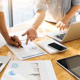 Zwei Personen sitzen an einem Tisch und schauen auf Papiere und einen Laptop.