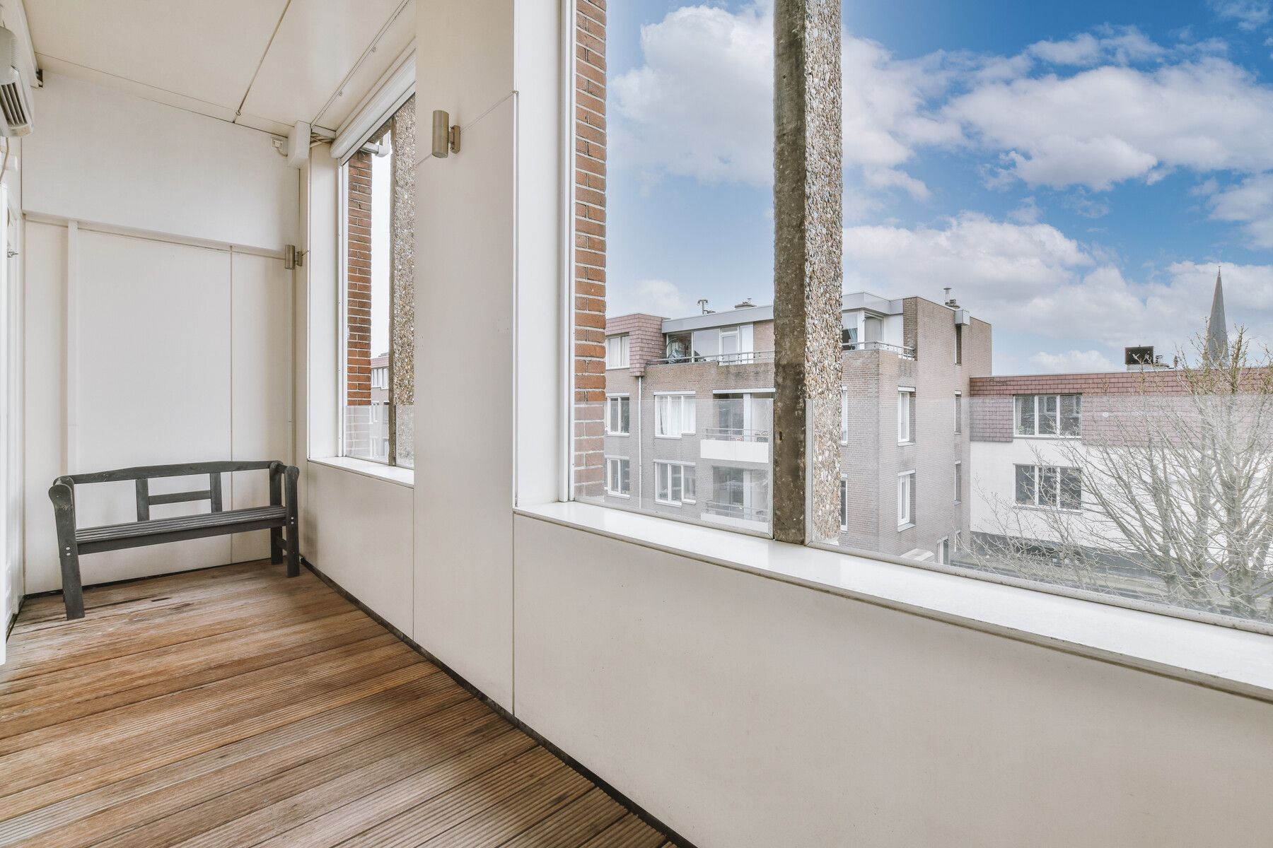 Un balcón con un banco y un gran ventanal con vistas a una ciudad.