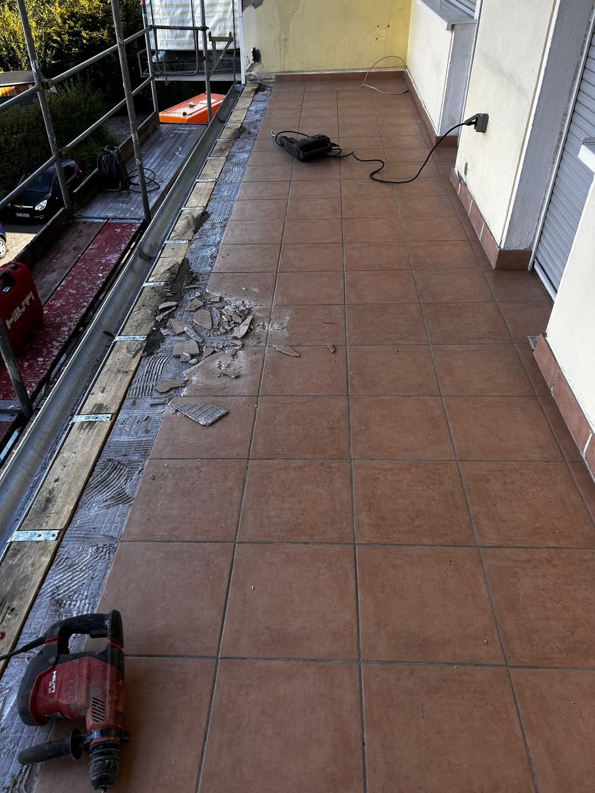 Balkon mit zerbrochenen Fliesen, Bauwerkzeugen. Gerüst, braune Fliesen.