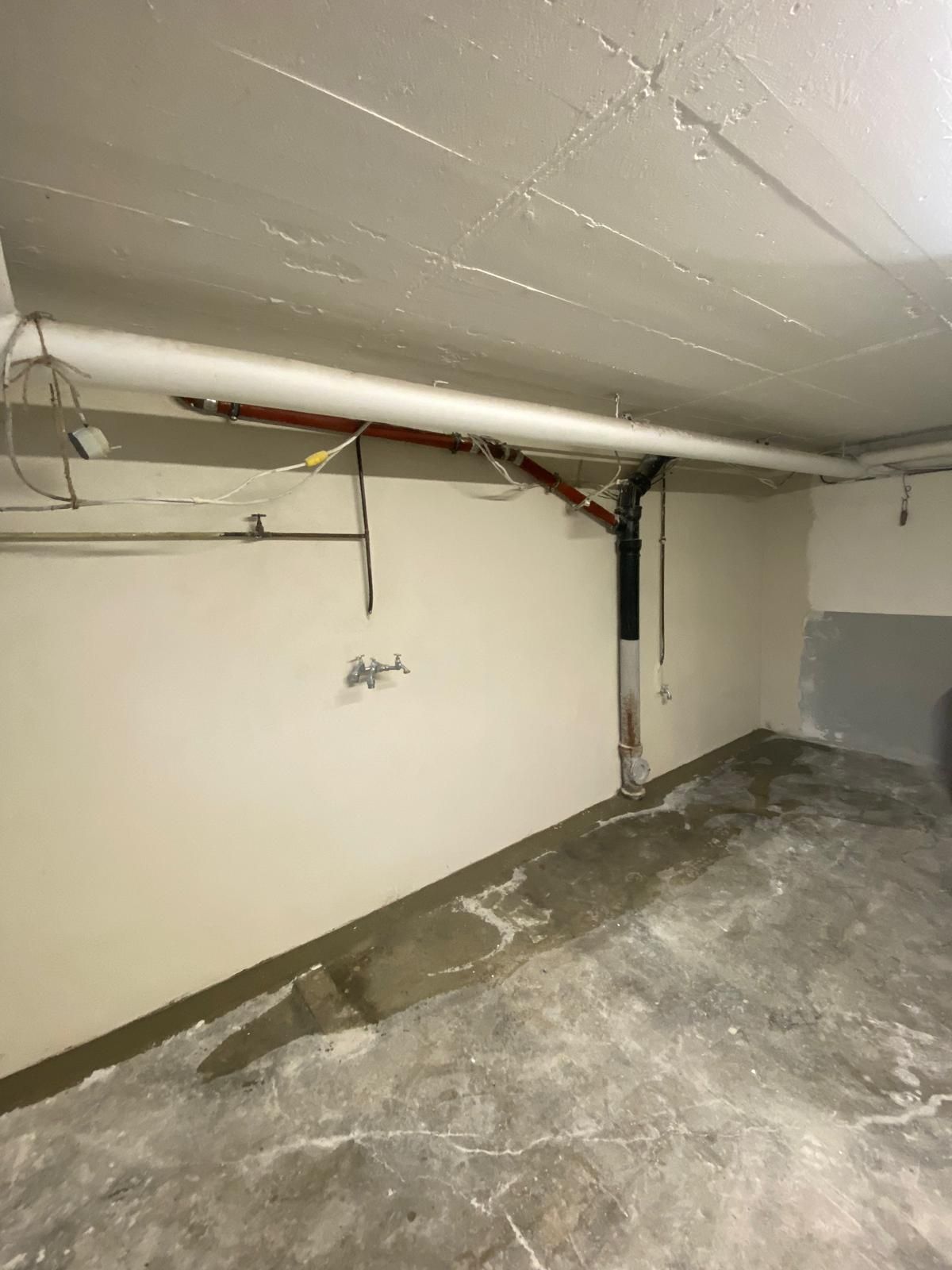Keller mit gerissenem Betonboden, Rohren an der Decke und einem Wasserleck.