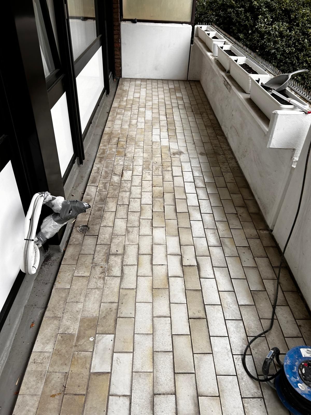 Mit Ziegeln gepflasterter Balkon, fleckig und schmutzig, mit weißer Wand und schwarzen Fensterrahmen und einem Stromkabel.