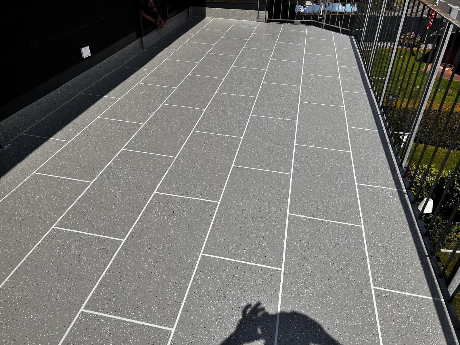 Grau gefliester Balkon mit schwarzem Geländer und hellem Sonnenlicht.