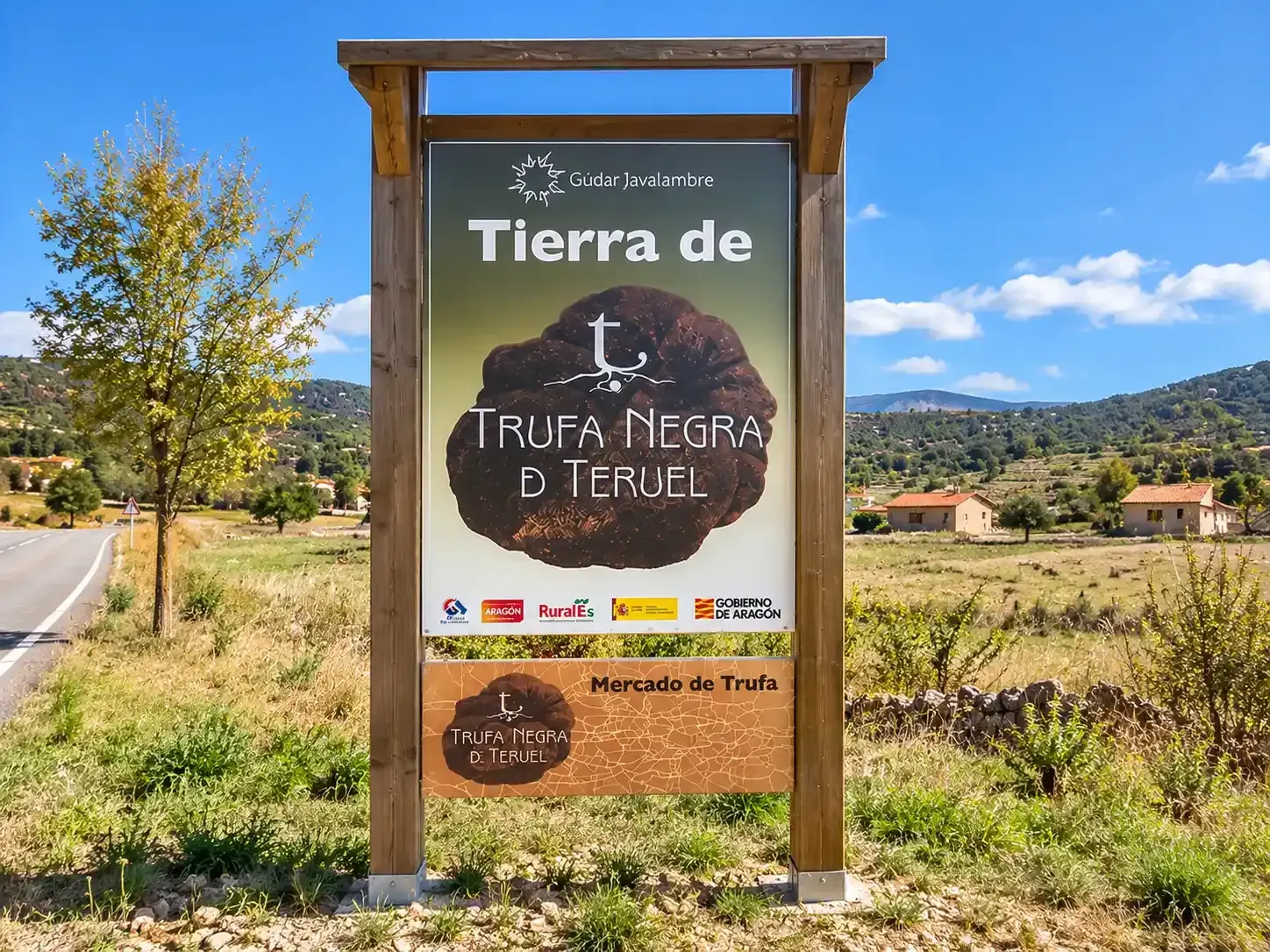 Señal de carretera que dice «Tierra de la Trufa Negra Teruel» en un paisaje rural bajo un cielo azul despejado