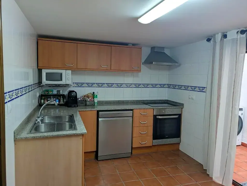 Cocina pequeña con armarios de madera, fregadero de acero inoxidable, horno, nevera y suelo de baldosas.