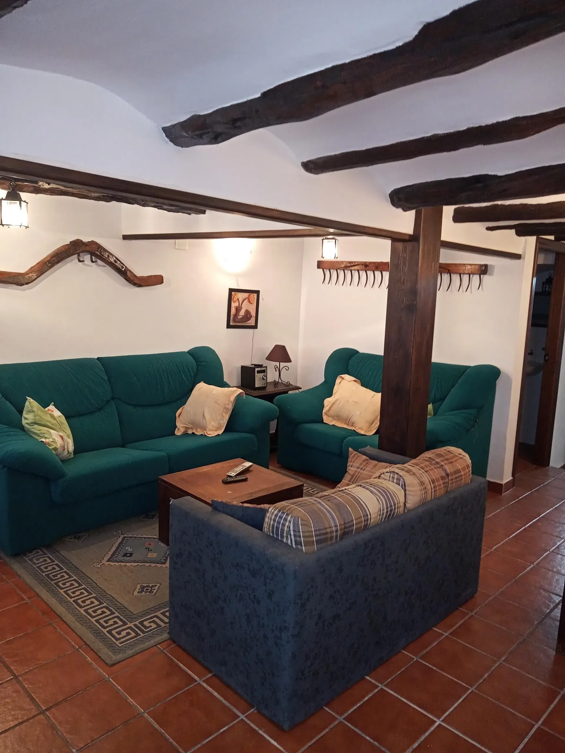 Acogedor salón con sofás verde azulado, sillón azul, vigas de madera y suelo de baldosas de terracota.