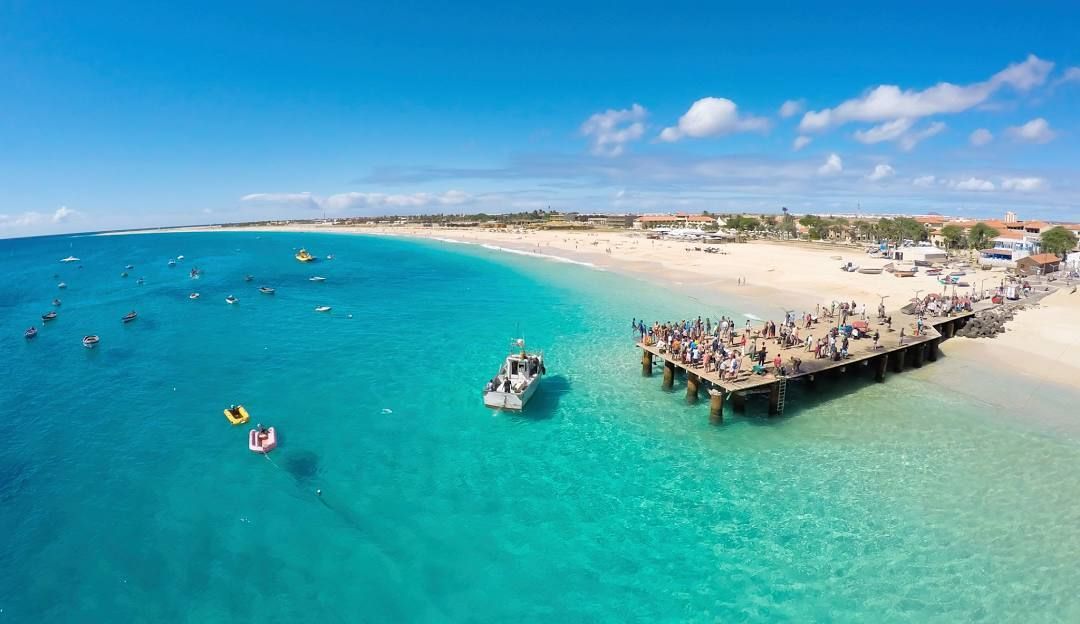 An aerial view of a beach with a pier and people swimming in the ocean.