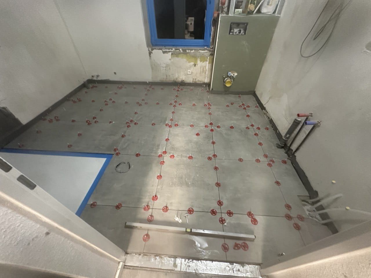 Badezimmerboden mit grauen Fliesen und roten Abstandshaltern, bereit zum Verfugen.