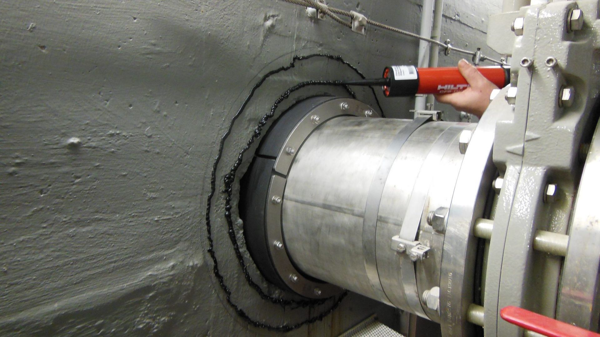 Eine Person bearbeitet mit einem roten Werkzeug ein Metallrohr.