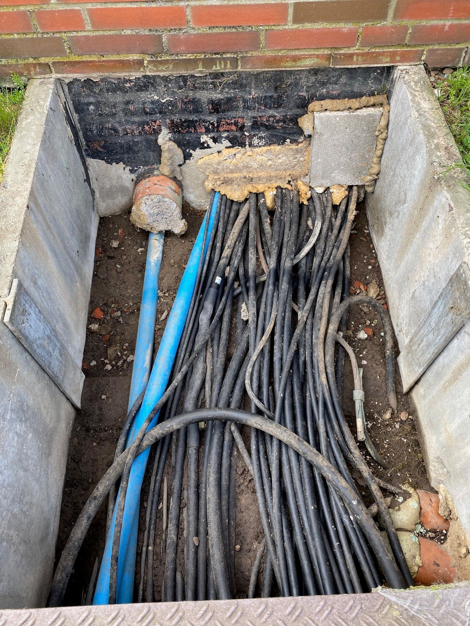 Ein Bündel Kabel liegt im Dreck in einem Betonkasten.