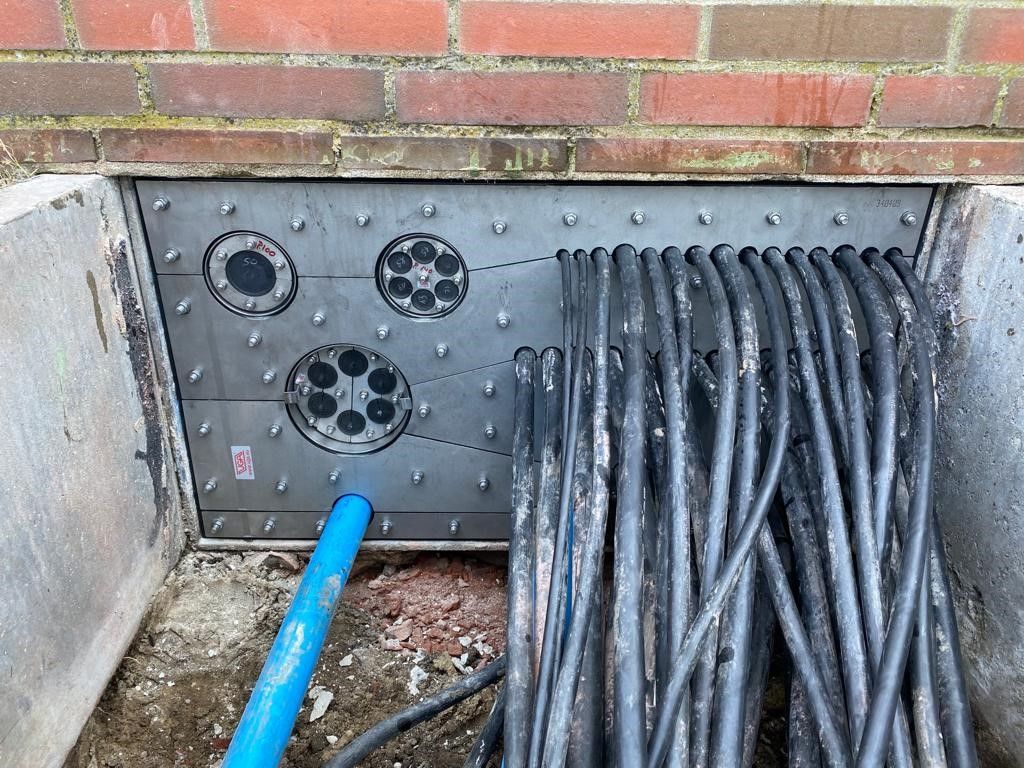 Ein Bündel Kabel liegt neben einer Backsteinmauer auf dem Boden.