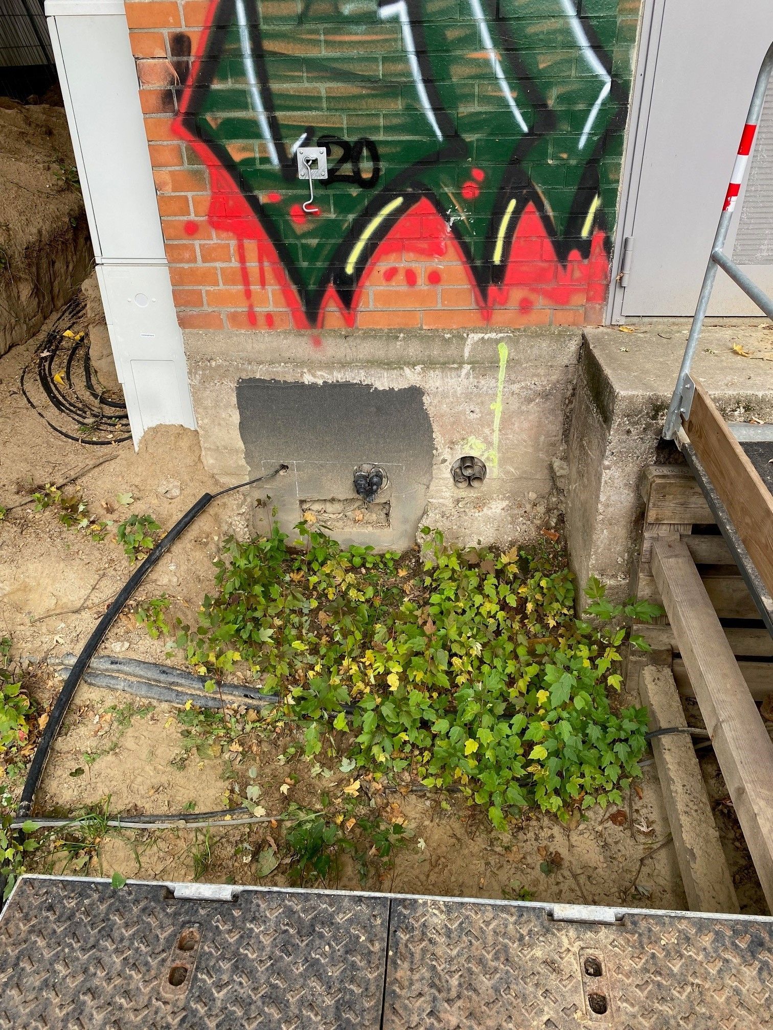 Ein Loch im Boden neben einer Backsteinmauer mit Graffiti darauf.