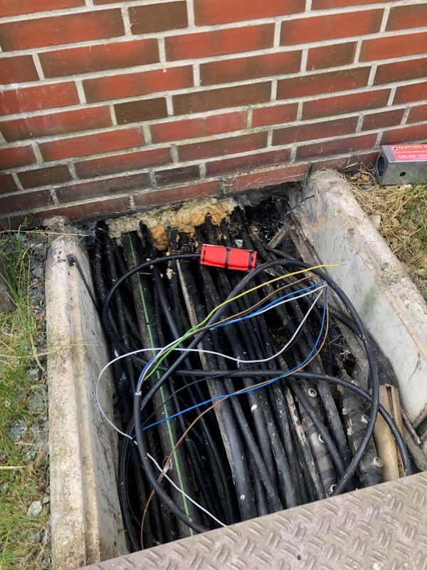Ein Bündel Drähte liegt in einem Loch im Boden neben einer Backsteinmauer.