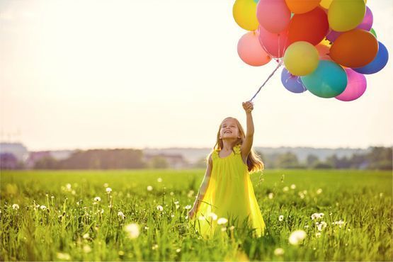 Una niña sostiene un montón de globos de colores en un campo.