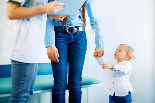 Una mujer sostiene la mano de un niño mientras habla con un médico.