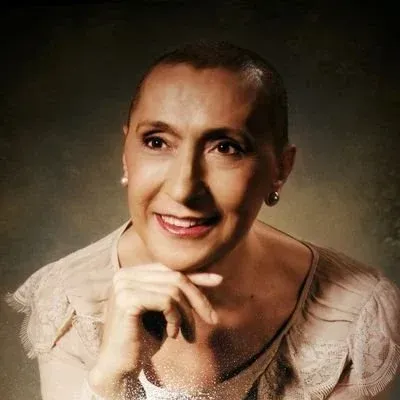 Retrato de una persona sonriente con cabello corto, apoyando la barbilla en una mano, sobre un fondo oscuro.