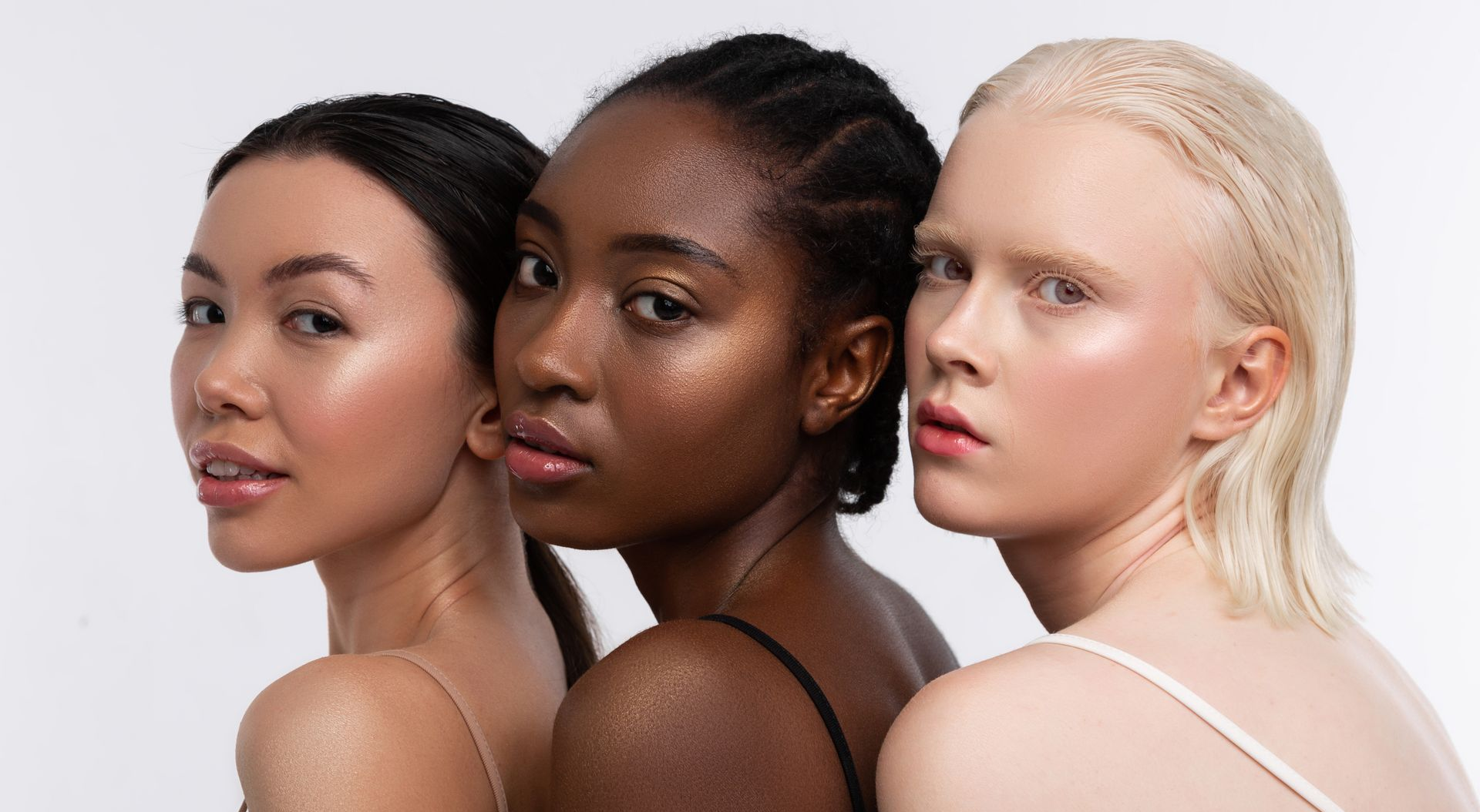 Trois femmes aux teints différents, regardant l'objectif, sur fond blanc.
