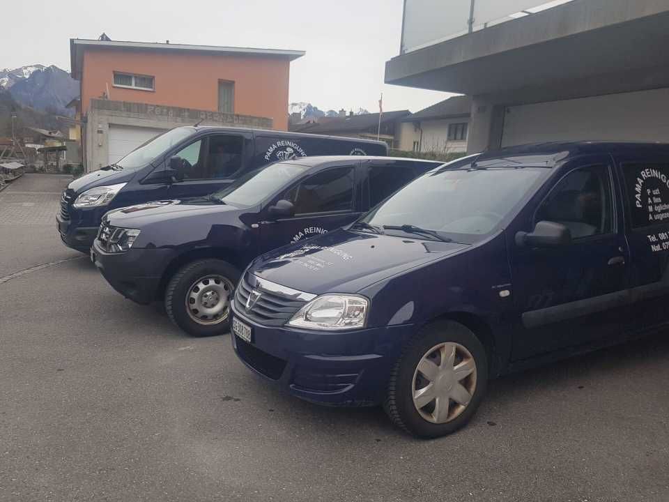 Drei dunkle Lieferwagen parkten auf einem Parkplatz neben einem orangefarbenen Gebäude und Bergen.
