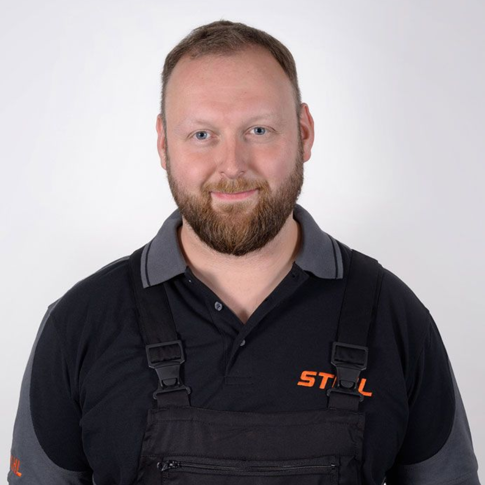 Mann mit Bart, der ein schwarzes Hemd und eine Latzhose mit dem