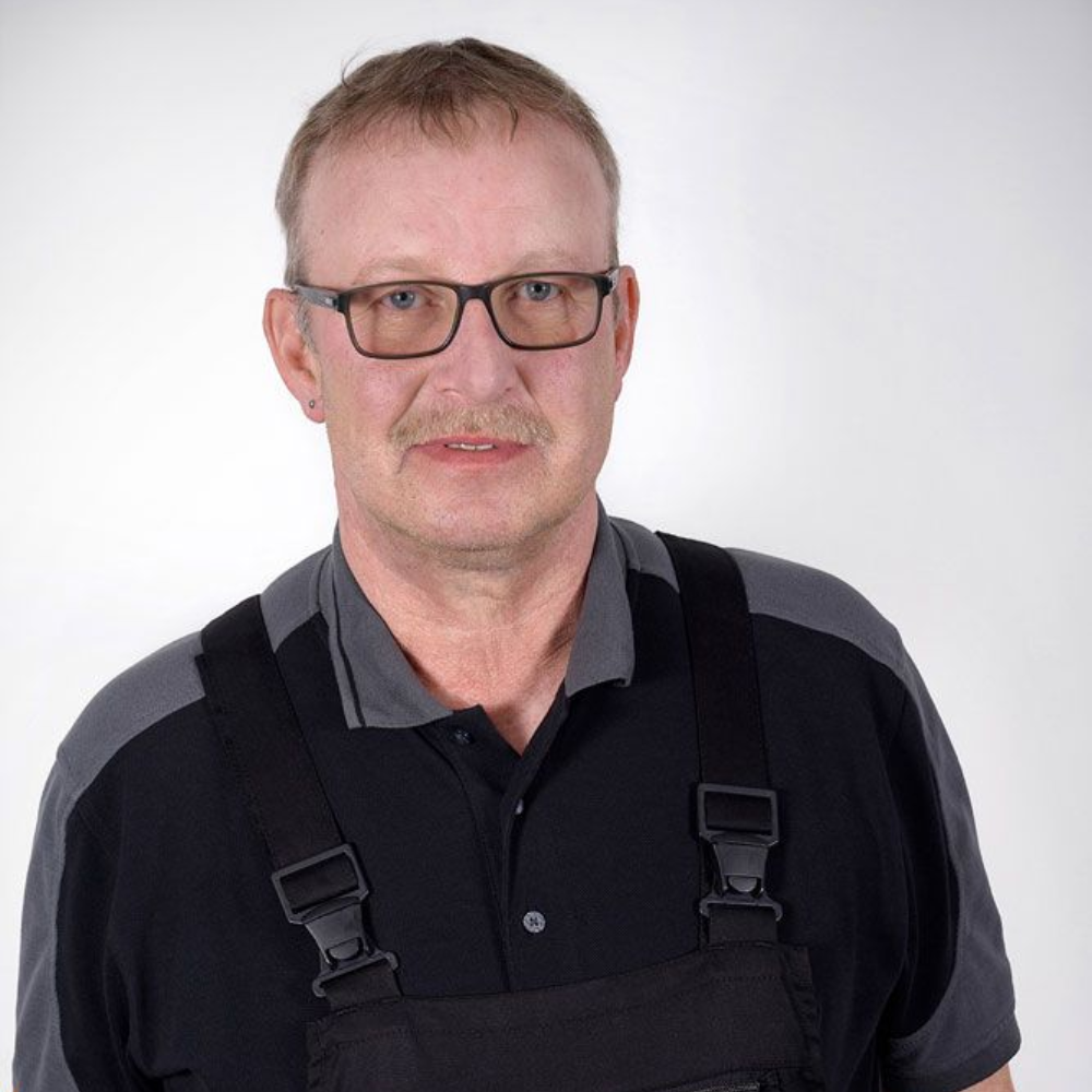 Mann mit Brille und Arbeitsoverall, der in die Kamera schaut.