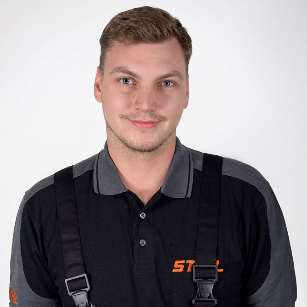 Ein Mann in einem Stihl-Arbeitshemd mit Hosenträgern lächelt vor einem weißen Hintergrund in die Kamera.