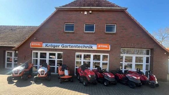 Vor einem Backsteingebäude parken mehrere Rasenmäher.
