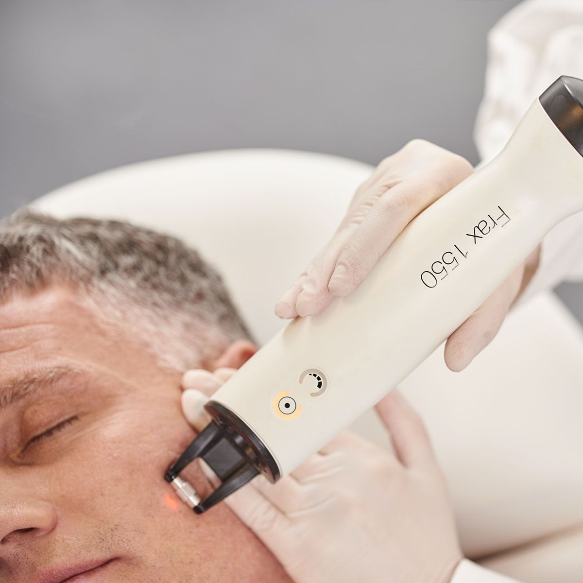 Persona que recibe un tratamiento láser facial con un dispositivo blanco en la mejilla; en el interior.