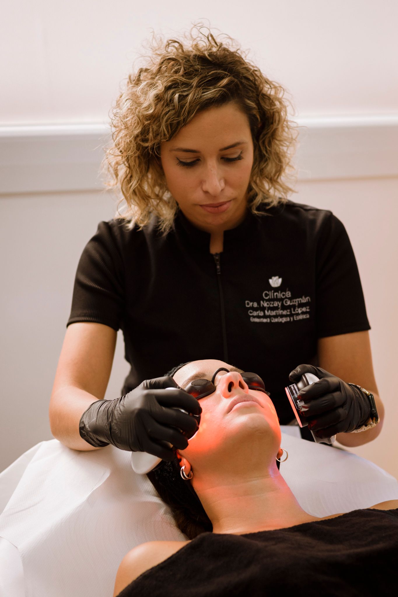 Mujer realizando un tratamiento facial con luz roja a otra mujer en un entorno médico.